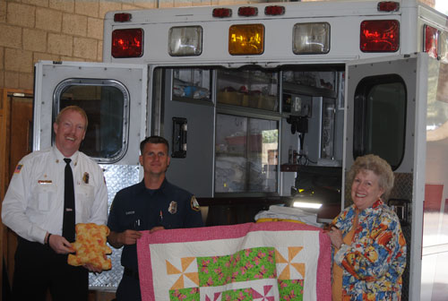 Each year, the Mountain Quilters of Idyllwild make about 40 to 50 security quilts, which are given to the Idyllwild HELP Center, the California Highway Patrol and the Idyllwild Fire Department for fire victims and the needy. This year they are also making stuffed bears. Idyllwild Fire Chief Patrick Reitz (left), holds the bear, and Firefighter Greg Minor (center) accepts a quilt and bear from Joyce Cummings, chair of the Security Quilt Committee. Photo by J.P. Crumrine