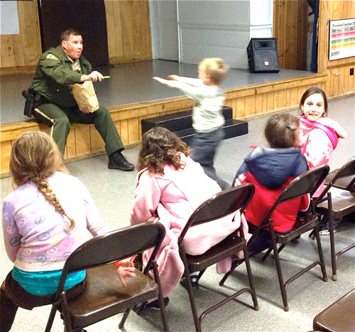 Riverside County Sheriff’s Deputy Waters rewards Idyllwild youngsters who have good answers at Town Hall while talking with them and their parents about strangers. Photo by Jack Clark