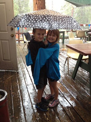 Carter and Evelyn Johnson share an umbrella during the thunderstorm Saturday while enjoying the Sons of the American Legion Post 800 Horseshoe Tournament.  Photo by Halie Wilson