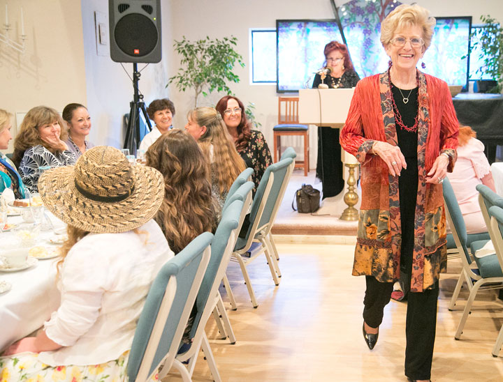 TEA & FASHION: Sunday afternoon, Marion Young (right) models an outfit during the High Tea and Fashion Show fundraiser for the Spiritual Living Center, which was sponsored by Prairie Dove. Phyllis Brown, owner of Prairie Dove, is shown at the podium.        Photo by Jenny Kirchner 