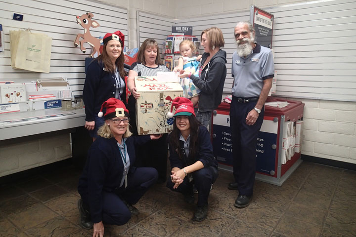 NORTH POLE MAIL: Evelyn Teel, 3, is the first to drop her letter to Santa in the North Pole-bound mail box at the Idyllwild Post Office. Helping Santa are post office employees Julie Stanford and Christina Reitz (front), Kelsi Lehman, Postmaster Kelly Gates, Mom Theresa Teel and John Aussenhofer. The mail box will be in the Idyllwild Post Office lobby until Friday, Dec. 12, for children to send Santa their Christmas wishes. Santa allows the Town Crier to print the letters in the Christmas edition for readers to enjoy. Photo by Halie Wilson