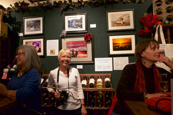 ART SHOW OPENING: Kathy Keane (center) stands among her friends and photography at the opening of her exhibit on display at Idyll Awhile Monday night. Photo by John Drake