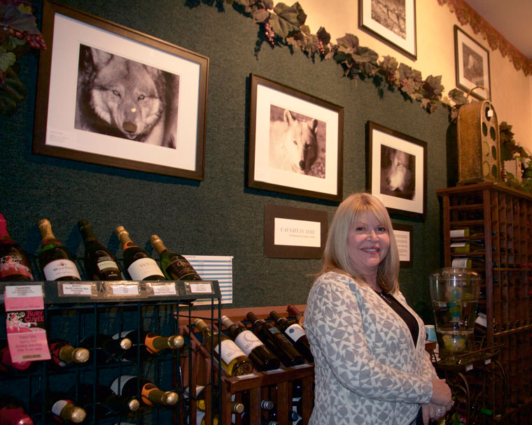 Photographer Susan White stands next to a triplet of wolves at her artist reception Thursday night. Her collection of black and white photographs, “Caught in Time,” is now on display at Idyll Awhile Wine Shoppe Bistro. Photo by John Drake