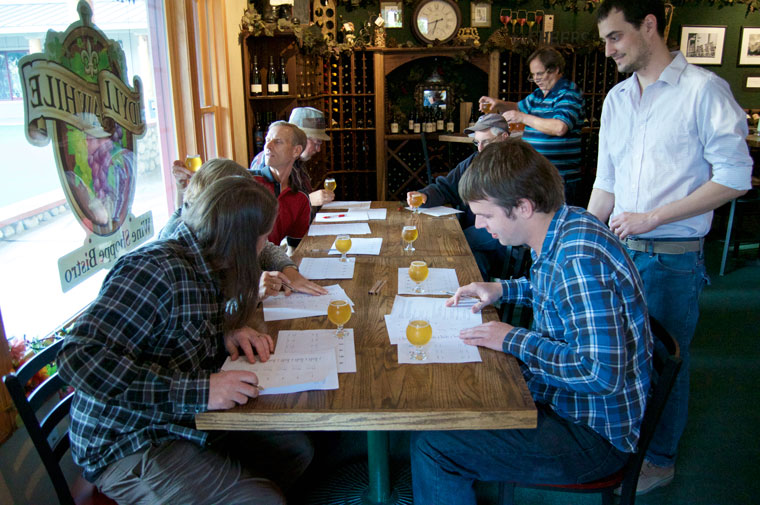 Aaron Erlandson (second from right) rates the first beer given at Idyll Awhile Wine Shoppe Bistro’s beer tasting last week. Distributing the samples are Jared Dillon (standing right) and Dave Dillon (standing behind), owner. Photo by Gallagher Goodland 