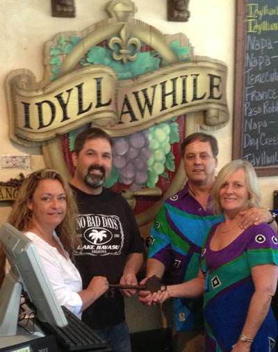 An ownership change for Idyllwild Awhile Wine Shoppe & Bistro occurs this week. The new owners, Lynn and Greg Adams (left), receive the key to the bistro from the original owners, Dave and Julie Dillon (right) over the weekend. Photo by J.P. Crumrine
