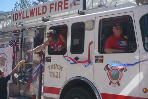 Rachel Teeguarden distributes flags from the Idyllwild Fire Department’s ladder truck and Jerry Buchanan, president of the Idyllwild Fire Protection District commission, enjoys the ride. Photo by Chandra Levy