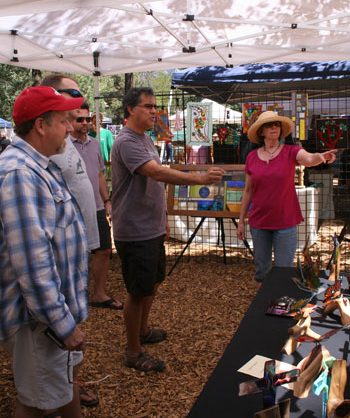Kim Finnell (right) explains to art enthusiasts how her husband Scott Finnell creates his stained-glass work on Saturday at Art in the Park.Photo by Becky Clark 