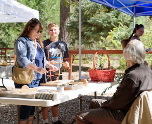 Sandy Ezell (left) of Idyllwild and grandson Robert Martinez of Hemet work at drilling holes using tools similar to those the Cahuilla people used when they occupied the site of the Idyllwild Nature Center. The center hosted the annual “Trail of the Acorn” event. George Ray (right) provided the equipment and instruction as part of the demonstration, which offered a look at the life of the nomads as they followed the plants that were in season between the desert and mountains. Photo by Tom Kluzak