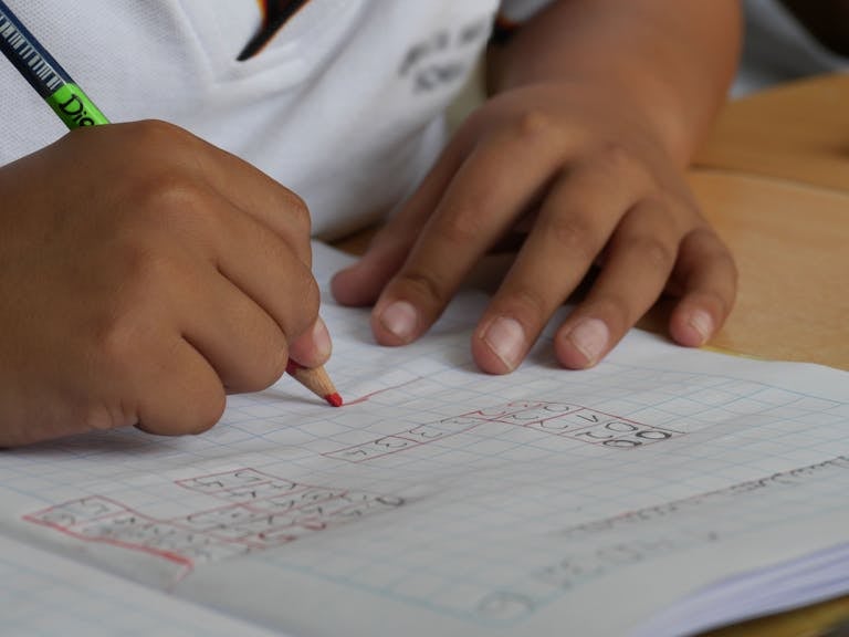 Close-up of a student writing math equations in a notebook with a pencil indoors.