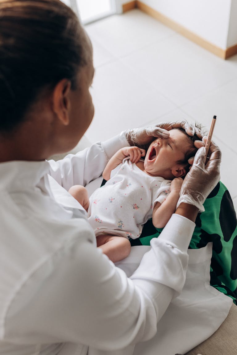 A newborn baby yawns during a health checkup by a doctor in a clinical setting.