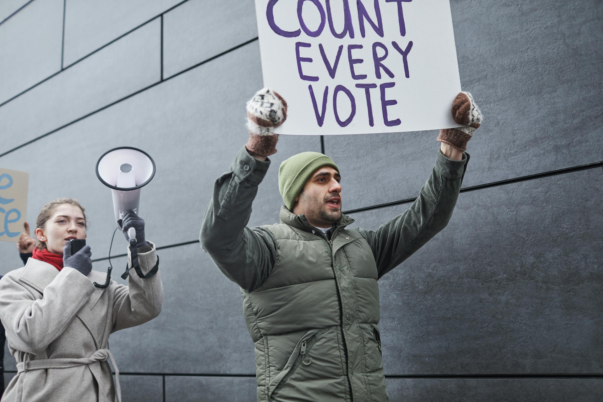 Protesters holding signs and a megaphone, demanding every vote to be counted during a winter rally.