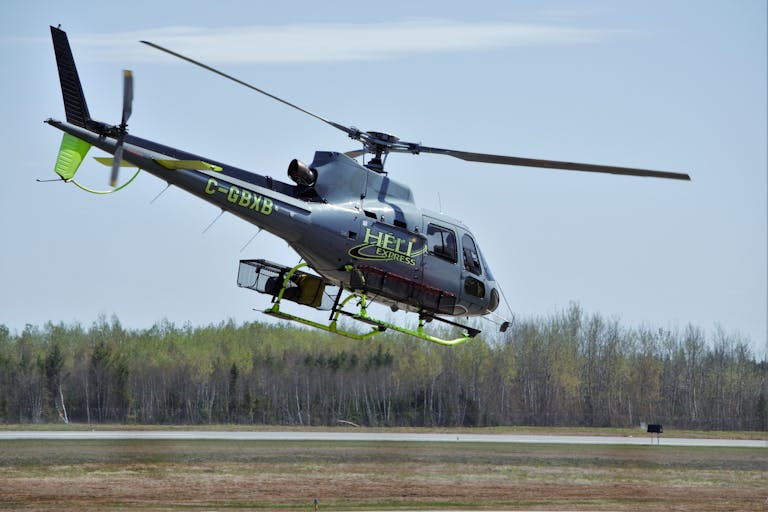 Helicopter mid-flight over a forest on a clear day, showcasing agility and speed.