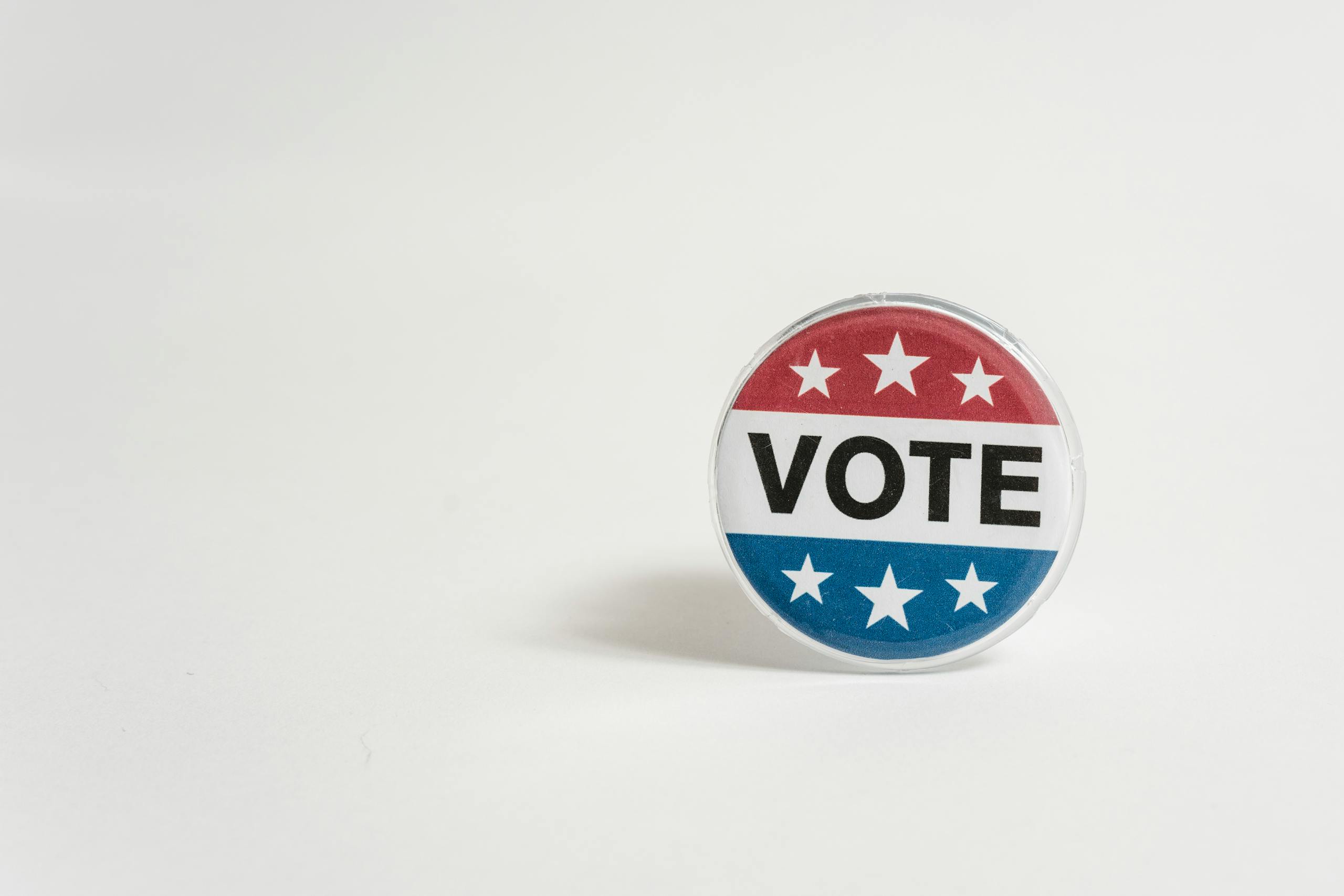 Close-up of a red, white, and blue vote button with stars on a white background.