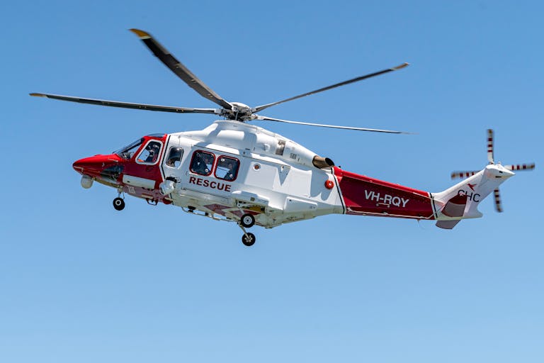 Red and white rescue helicopter with visible rotors flying against a clear blue sky.