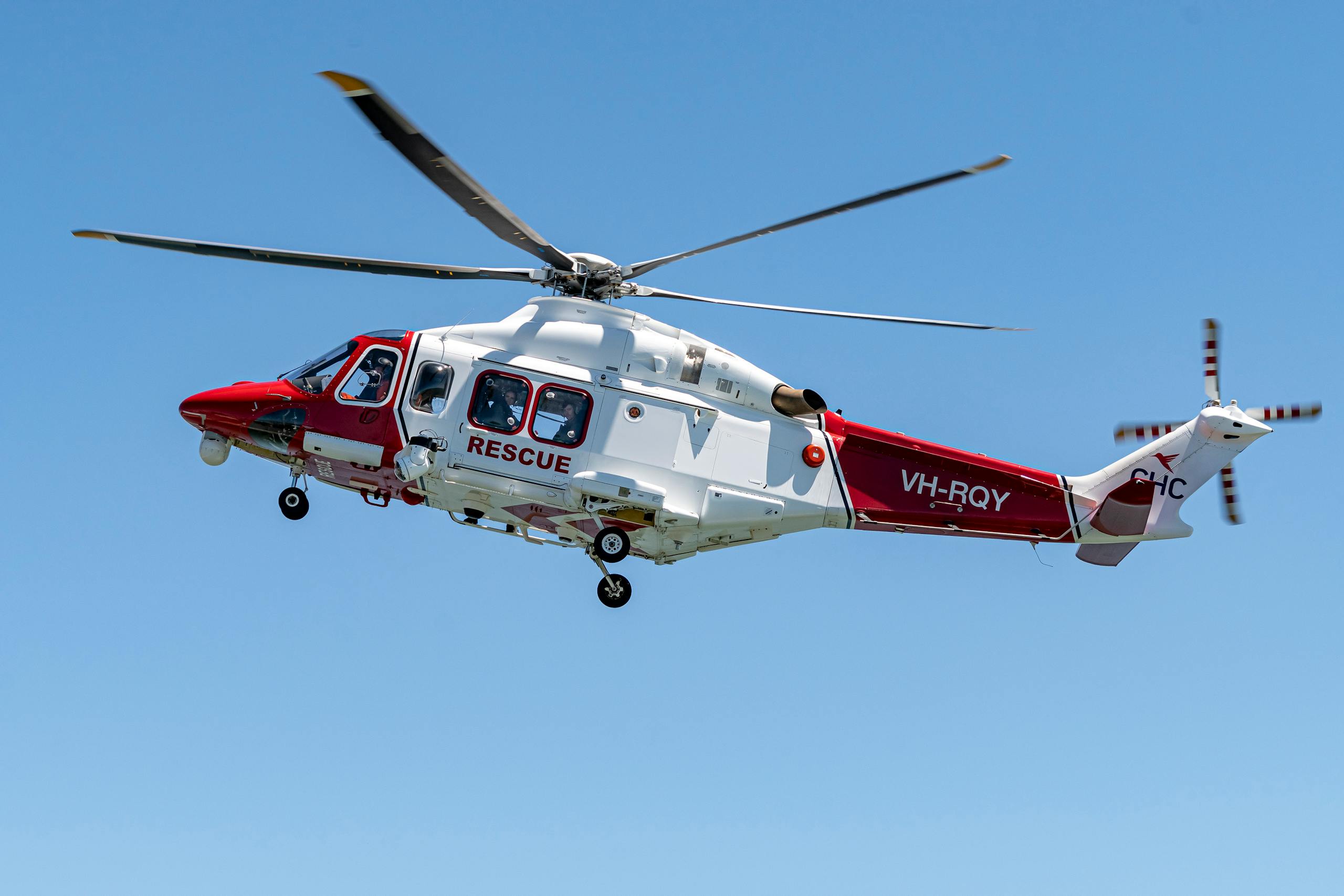 Red and white rescue helicopter with visible rotors flying against a clear blue sky.