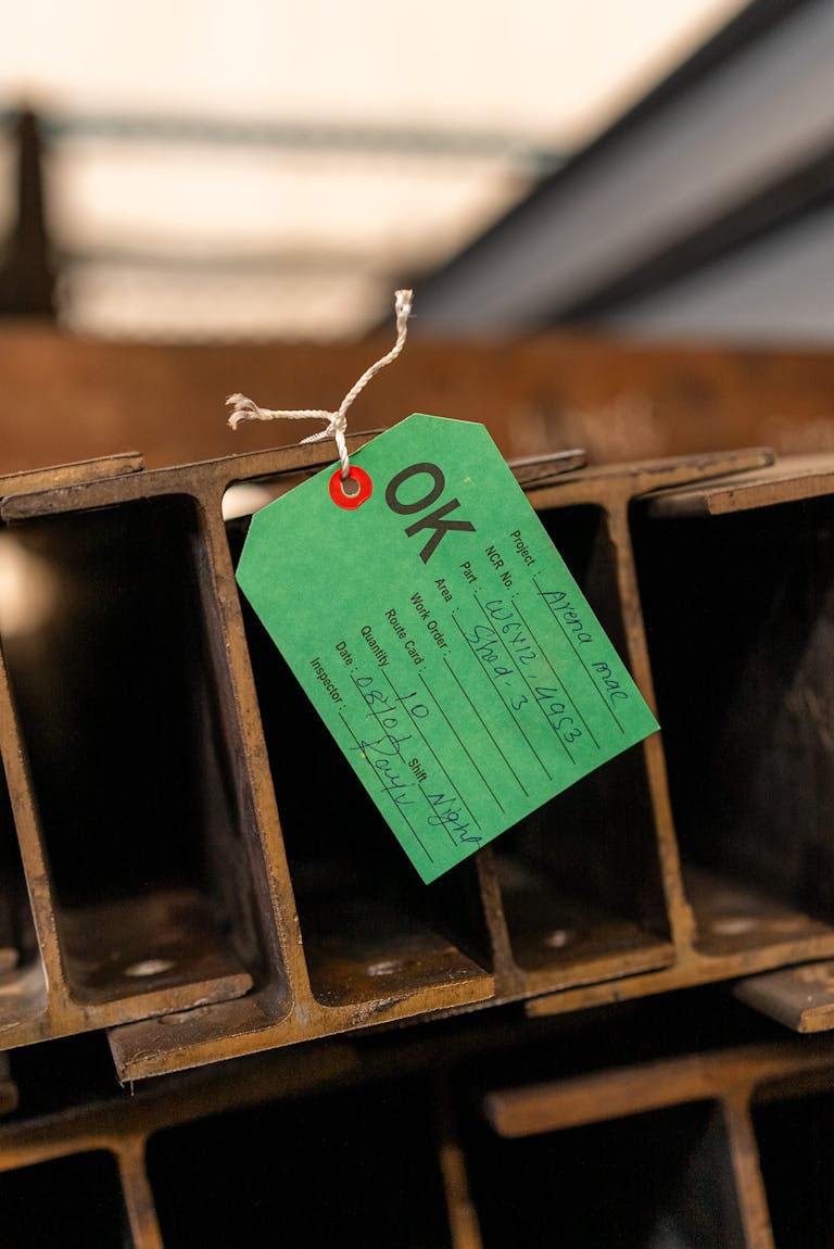 Close-up of a steel beam with an attached inspection tag in an industrial setting.