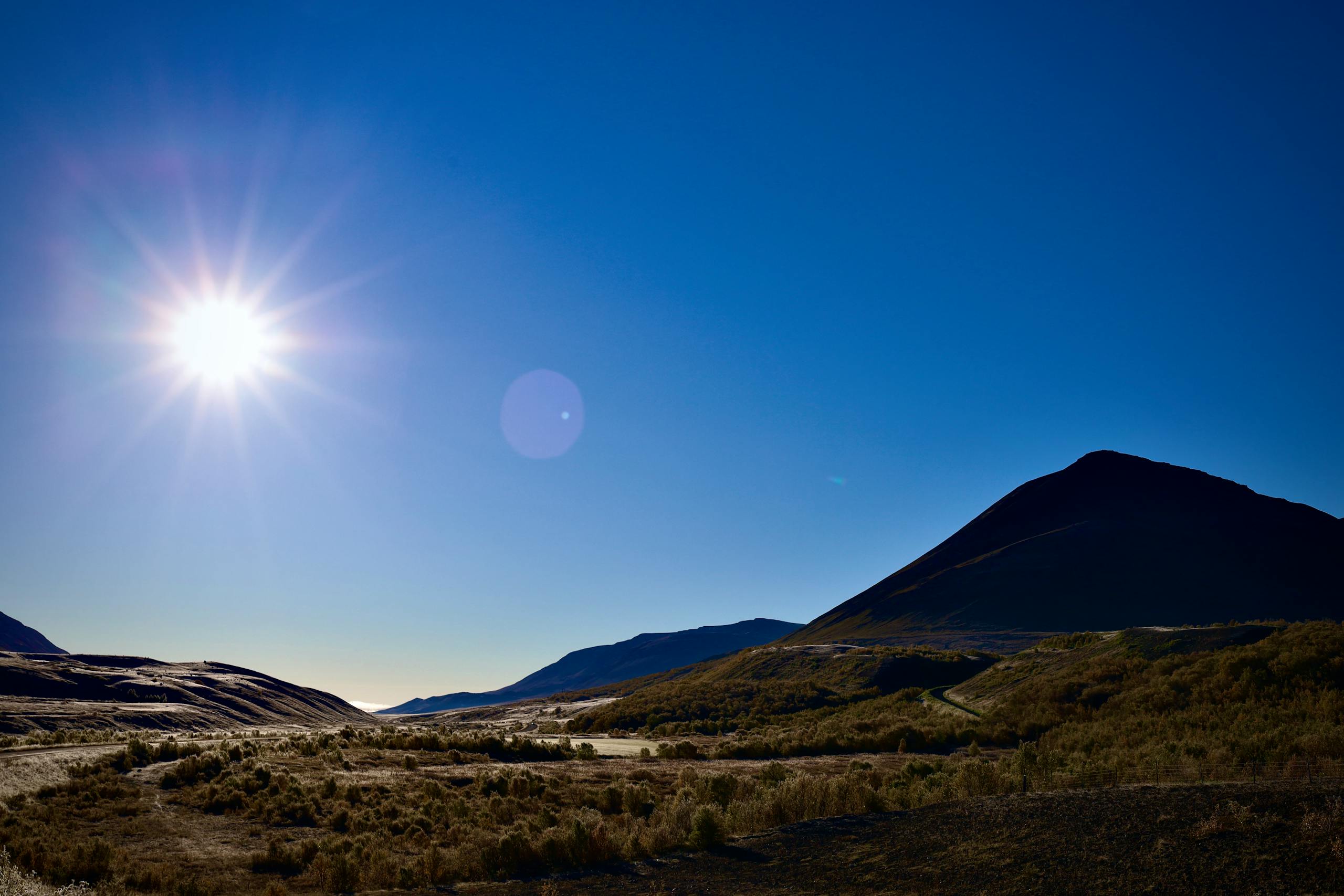 Vibrant mountain landscape with bright sun and clear blue sky, capturing natural beauty and tranquility.