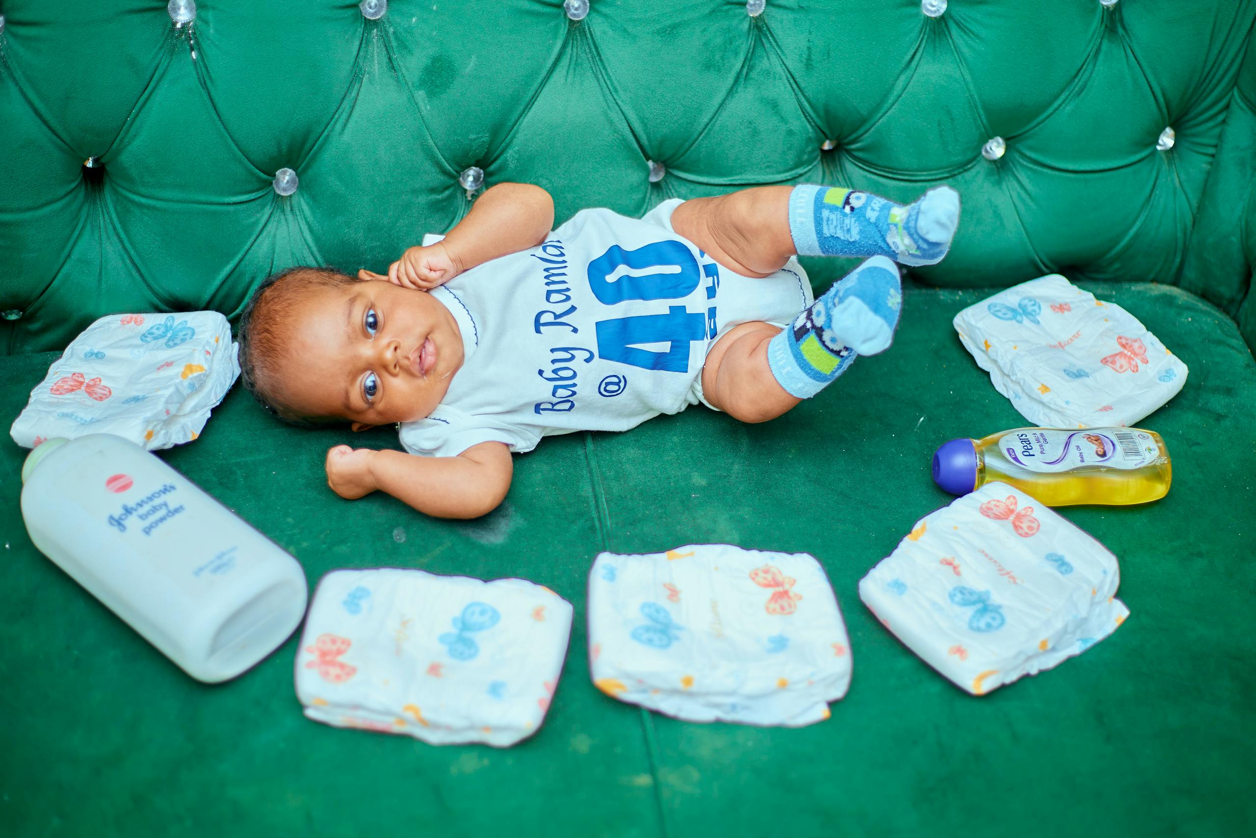 Cute baby lying on a green couch surrounded by diapers and baby care items