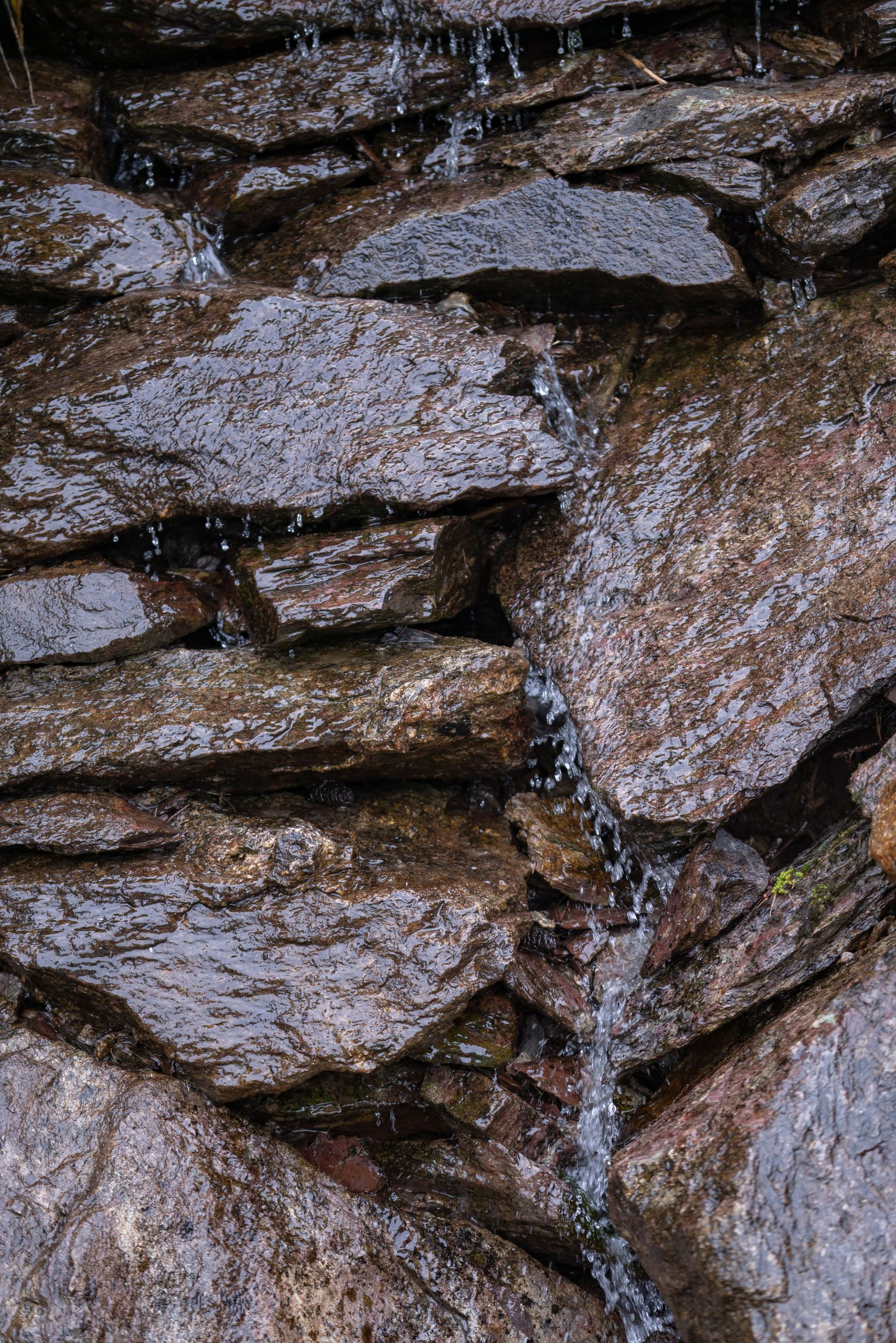 Close-up of wet rocks with water trickling down their surface creating a natural pattern.