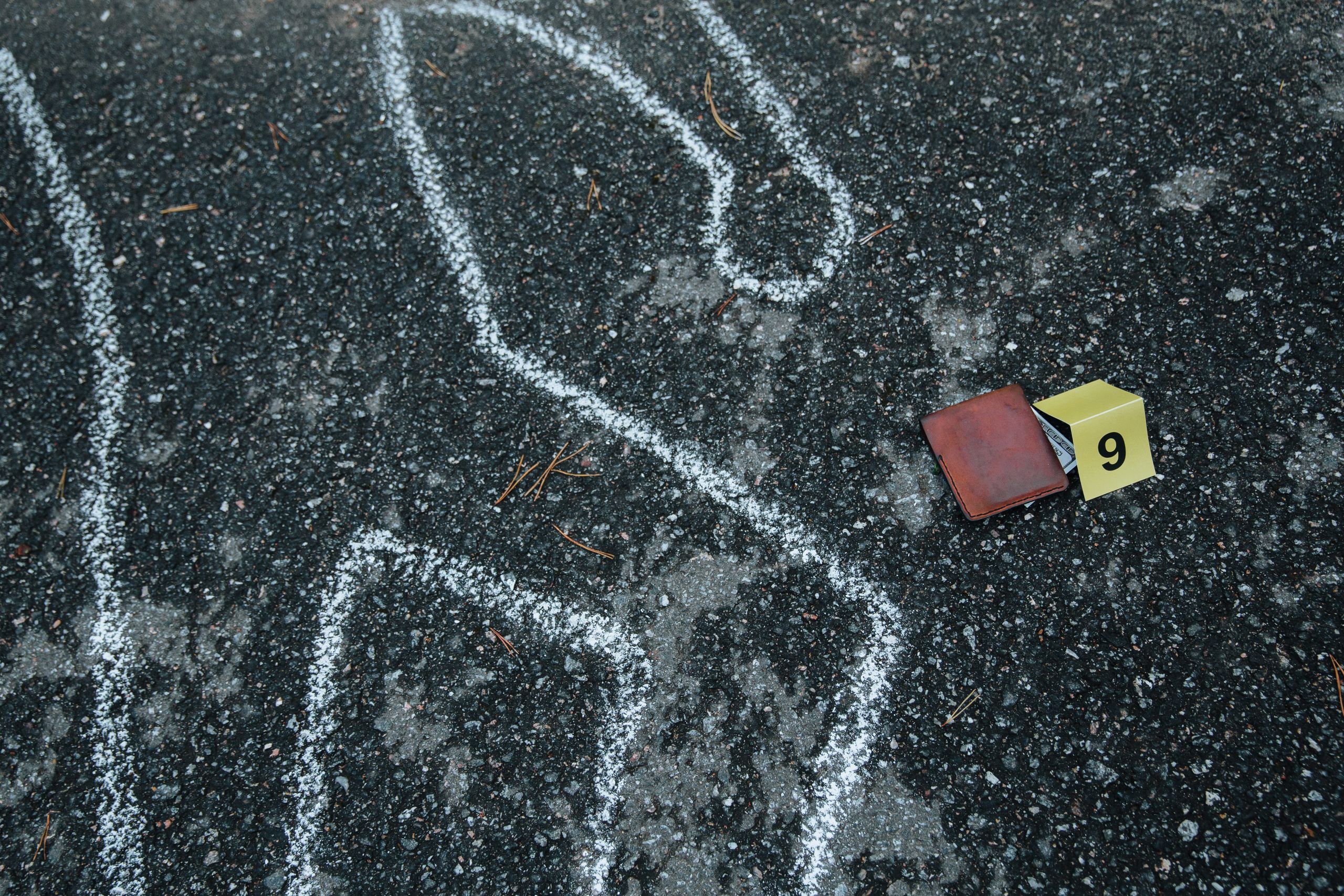 Crime scene with a chalk outline and evidence marker on asphalt.