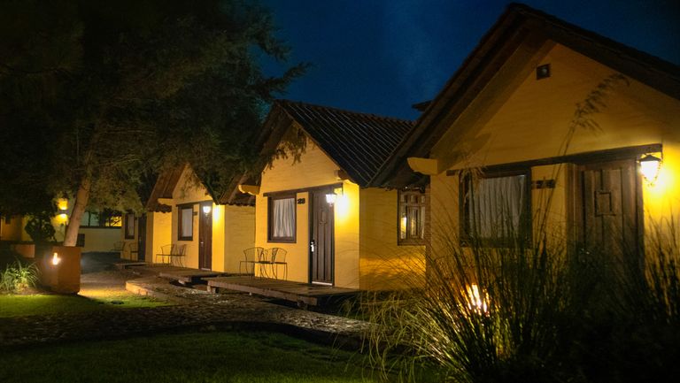 Rustic cabins warmly lit against a night sky, surrounded by greenery.