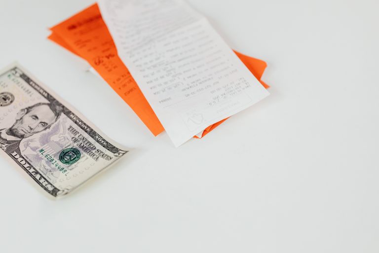 A five dollar bill and receipts on a white surface, emphasizing finance and expenses.