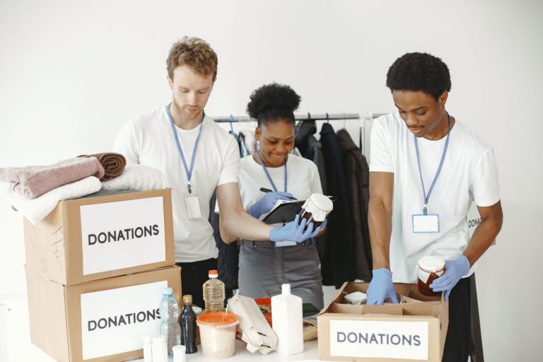 Stock photo for illustration: Three volunteers organizing donation boxes with clothes and food items in a community center.