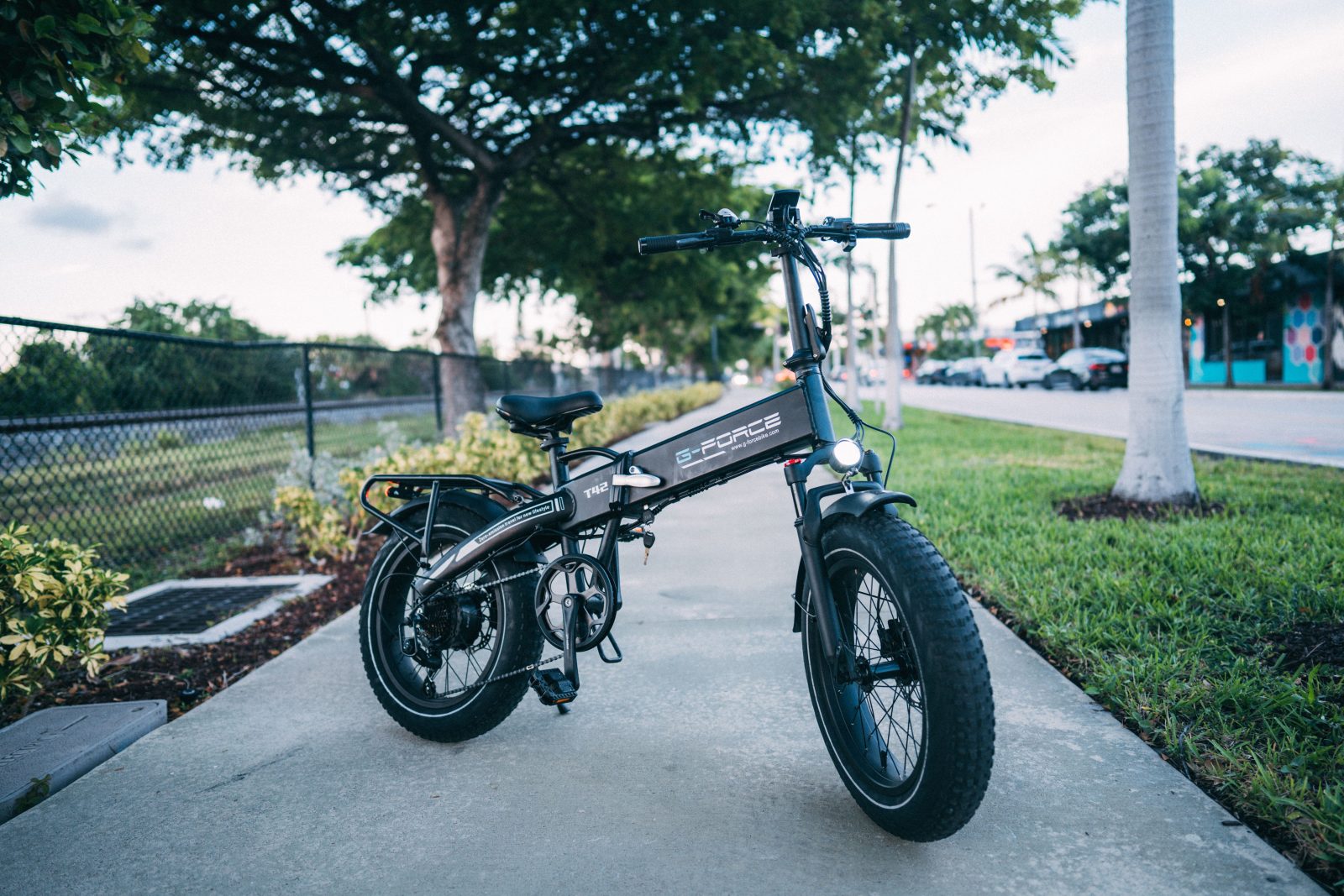 Stock photo for illustration: Sleek electric bike parked on a city sidewalk surrounded by greenery.