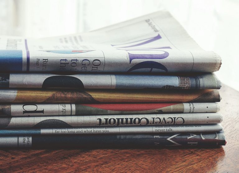Stock photo for illustration: A stack of folded newspapers placed on a wooden table, symbolizing news and information.