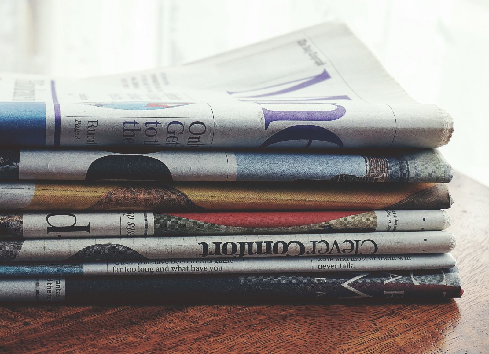 Stock photo for illustration: A stack of folded newspapers placed on a wooden table, symbolizing news and information.