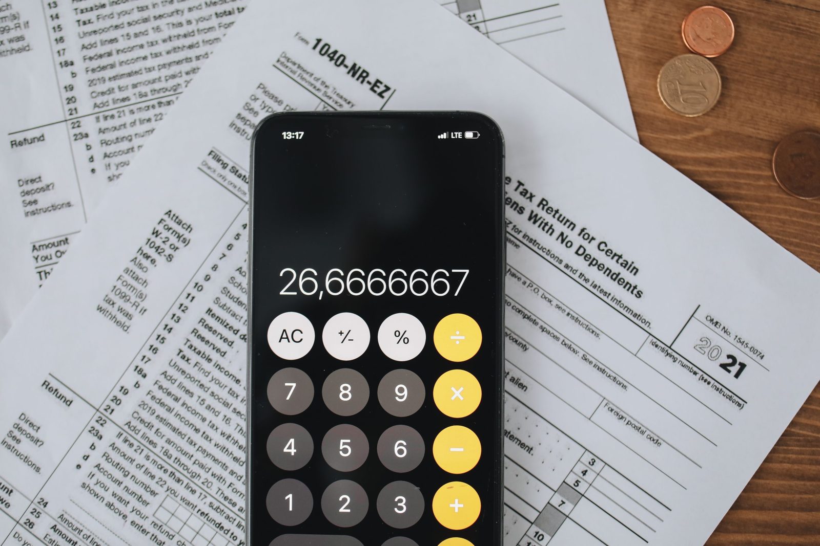 Stock photo for illustration: Smartphone calculator over tax forms with coins, symbolizing tax calculation and finance.