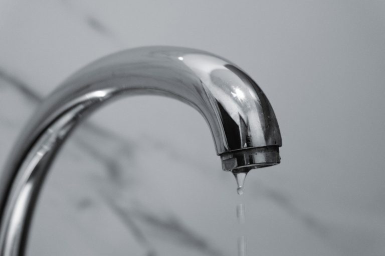 Stock photo for illustration: A close-up shot of a modern chrome bathroom faucet with water dripping from the tip.