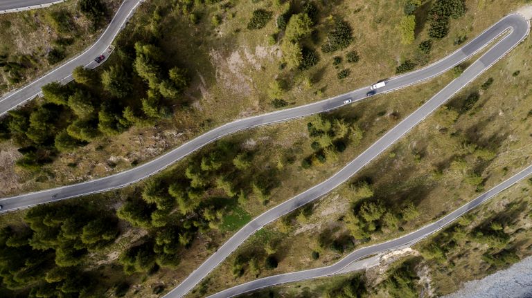 Top-down drone shot of a winding mountain road surrounded by green trees and natural scenery.
