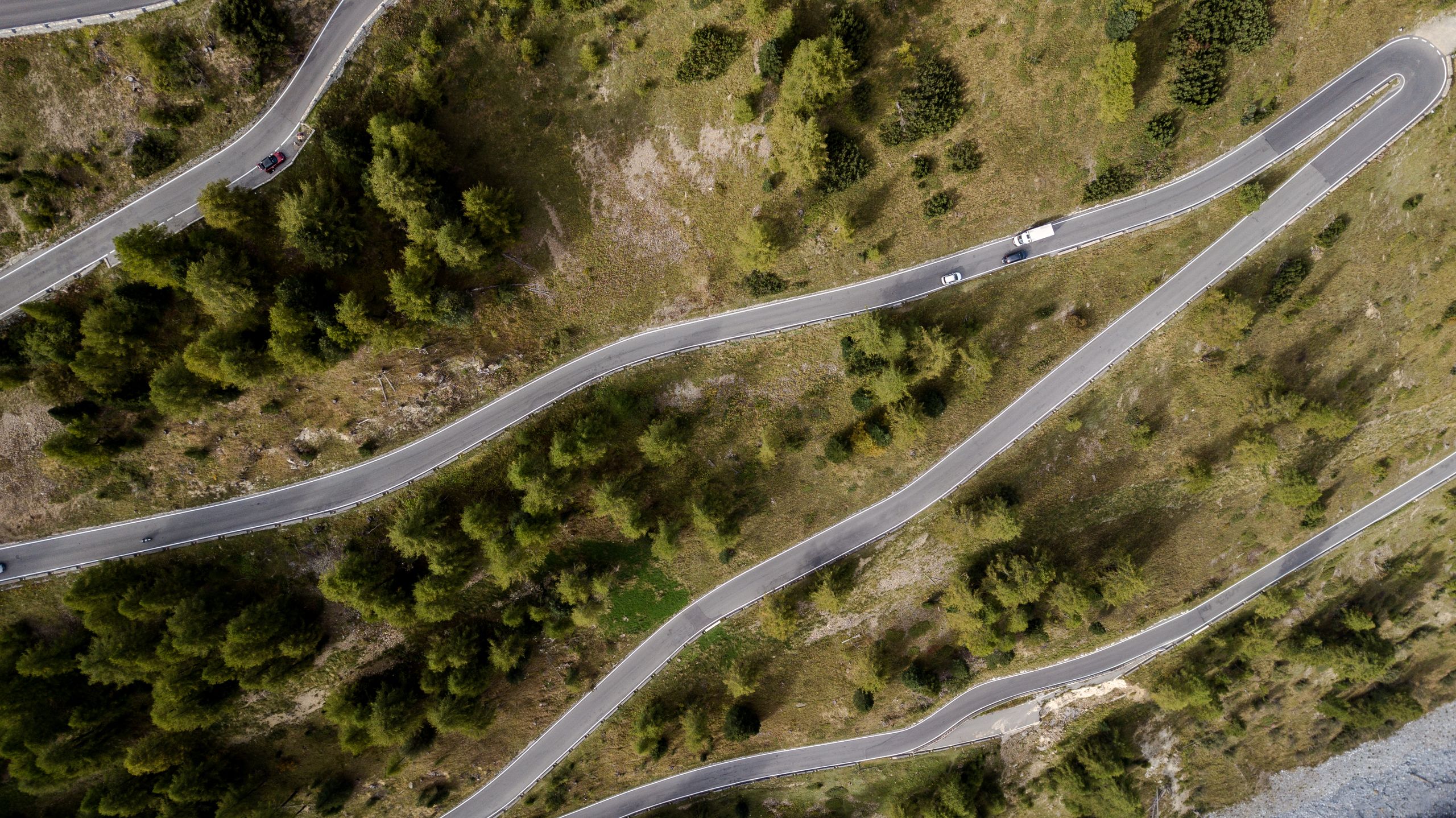 Top-down drone shot of a winding mountain road surrounded by green trees and natural scenery.